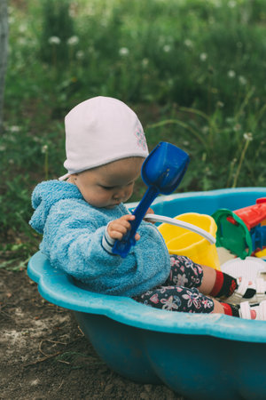 the child is sitting in the sandbox and playing in the sandbox toy balls, shovel, rakes and bucketsの写真素材