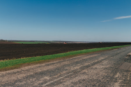 plowed field on which agricultural machinery rides. Summer day two tractors to plow, plow the soil on sloping, cornfield. Agricultural land treatment before planting.の写真素材