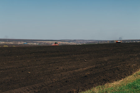 plowed field on which agricultural machinery rides. Summer day two tractors to plow, plow the soil on sloping, cornfield. Agricultural land treatment before planting.の写真素材