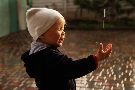 a small child catches raindrops, splashes fly into his face, closes his eyes. rainy weather. wet weather. acquaintance with the world. innocenceの写真素材