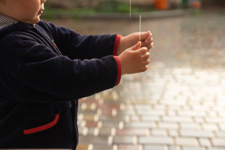 a small child catches raindrops, splashes fly into his face, closes his eyes. rainy weather. wet...