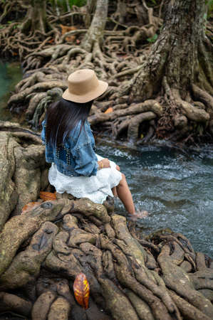 A woman swaying her feet in the water with the beautiful root of trees at Thapom Klong Song Nam, Krabi, Thailand.の写真素材