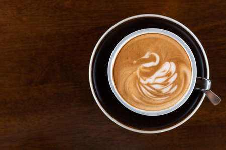 Latte art coffee with swan art in black cup on wooden tableの写真素材