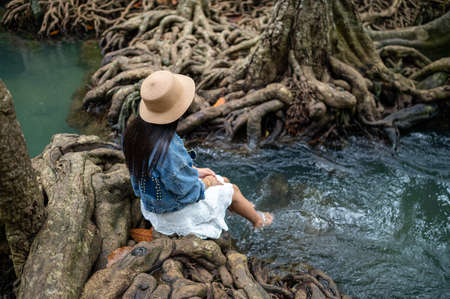 A woman swaying her feet in the water with the beautiful root of trees at Thapom Klong Song Nam, Krabi, Thailand.の写真素材