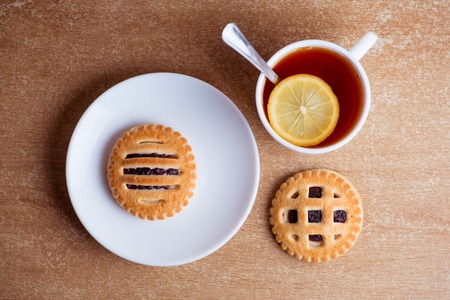 Cup of tea and lemon, cookies with jam in saucer on table top view.の写真素材