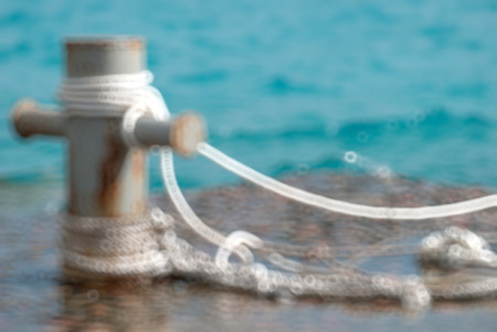 Rusty mooring bollard with ship ropes and clear turquouse sea ocen water, Blurred bokeh background.の写真素材