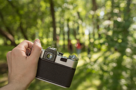 Man hand holding retro old film camera over bright sunny green forest blurred bokeh background. POV viewの写真素材