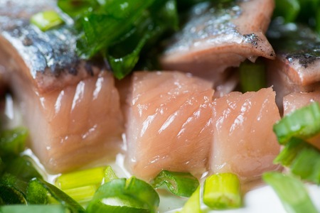 Sliced herring with green onion on a plate. Selective focus macro shot with shallow DOF.の写真素材