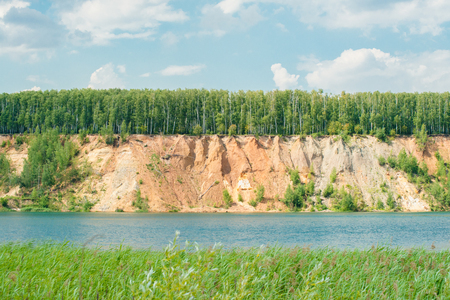 Blue lake with the orange yellow sand hills mountain and forest on top against skyの写真素材