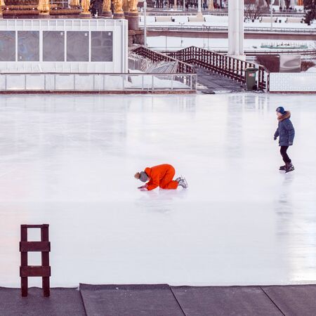 MOSCOW, RUSSIN FEDERATION - FEBRUARY 18, 2016: Girl and boy teenagers skating on the ice skate area placed on VDNKh in Moscow on winter sunny day, and she prepare kneeling for the ride.のeditorial素材