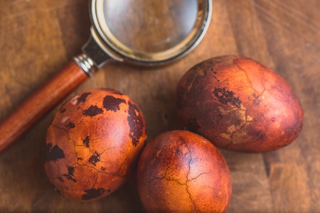 Easter eggs on wooden background. Painted brown with spots and cracks and magnify glass near....