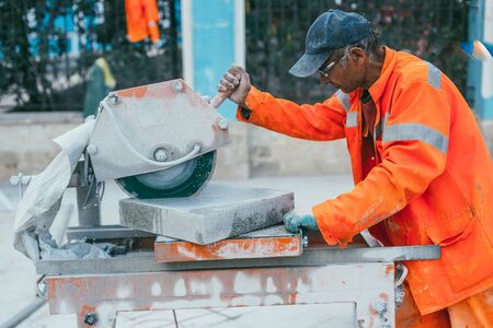 Moscow, Russia - August 14, 2015: a builder cuts a piece of granite stone on a circular saw machine. Reconstruction of pavement tiles in the capital near palace Chertkov House. Myasnitskaya streetのeditorial素材