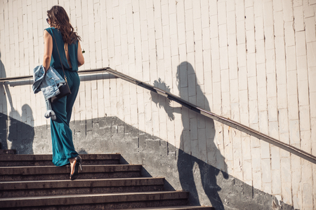 a girl in a beautiful green dress as an overalls holds flowers in her hands and goes up the steps from the underpass to the top. Frame in motionの写真素材