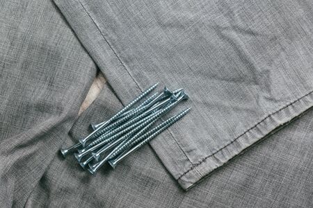 A handful of metallic self-cutters screws lies against the backdrop of an old denim fabric....