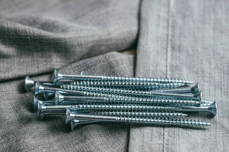 A handful of metallic self-cutters screws lies against the backdrop of an old denim fabric. Selective focus macro shot with shallow DOFの写真素材