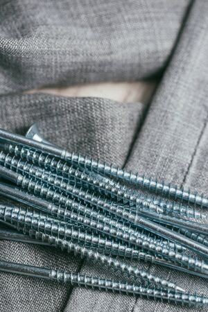 A handful of metallic self-cutters screws lies against the backdrop of an old denim fabric....