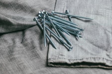 A handful of metallic self-cutters screws lies against the backdrop of an old denim fabric. Selective focus macro shot with shallow DOFの写真素材