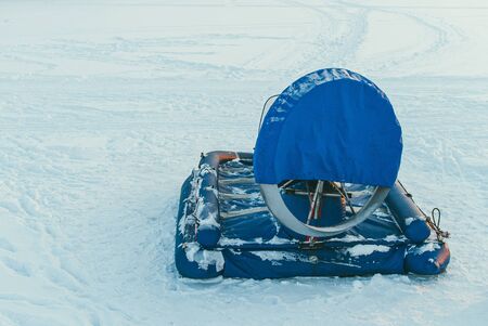 a hovercraft transport in blue protective covers stands on a frozen lake full of snow and ice. Copyspace for your text and designの写真素材