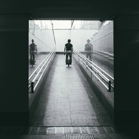 an unidentified middle-aged man rides a monocycle up a ramp in the underpass. Rear view. personal transport of the future. Black and white pictureの写真素材