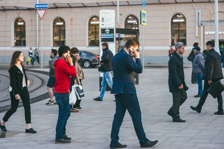 Moscow, Russia - may 25, 2017. A crowd of people of different genders and ages moves along the street in the pedestrian crossing area. Two men in the foreground are talking on the phone on the goのeditorial素材