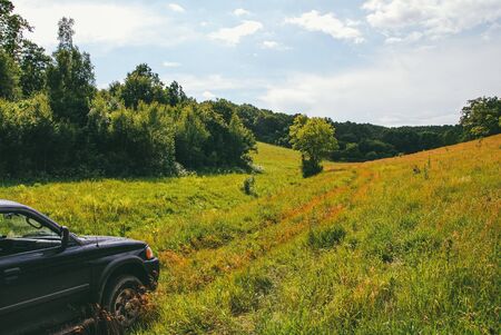 Travelers car in a field against the background of hills and spring forest. The concept of travel and adventure. Aerial view from the copterの写真素材