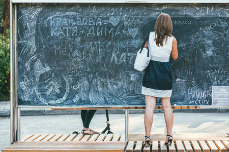 Moscow, Russia - AUGUST 9, 2014: Beautiful young girl in a short skirt and shoes writes on a chalk board in a park Sokolniki. Back view