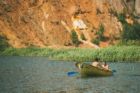 MOSCOW, RUSSIA JULY 06, 2014. Two men sit in a boat in lake against a background of sand rock and reedsのeditorial素材