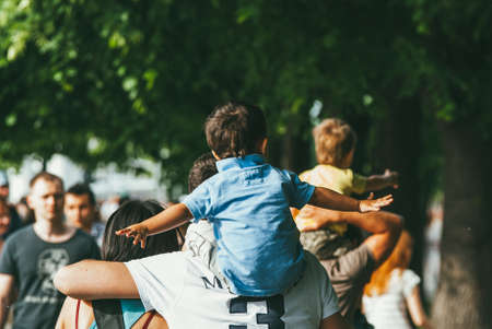 Moscow, Russia - June 1, 2014. Boys children sit on the necks of their fathers who walk in a crowd...