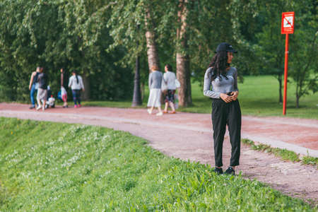 Moscow, Russia - JULY 11, 2017: A girl of Asian appearance in black sweatpants and a black baseball cap walks in Tsaritsino Park and enjoys nature against the background of a sign it is forbidden to swimのeditorial素材
