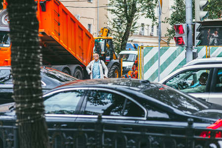 Moscow, Russia - JULY 7, 2017: An elderly man waits for the traffic light to pass on a pedestrian. Heavy traffic from cars In the foreground, construction equipment and workers in the backgroundのeditorial素材