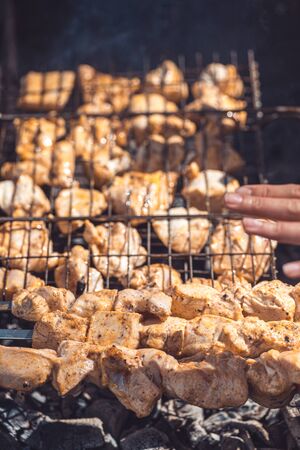A womans hand checks the degree of readiness of a barbecue cooked on coals, under the rays of the summer sunの写真素材