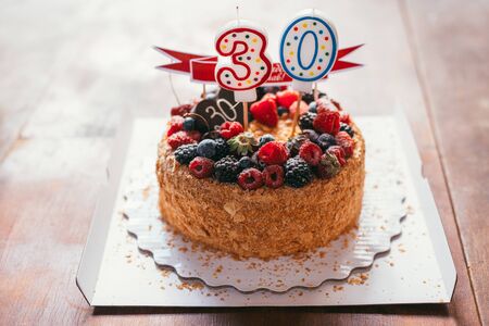 raspberries blackberry birthday cake with candles number 30 on defocused background with wooden table. Selective focus macro shot with shallow DOFの写真素材