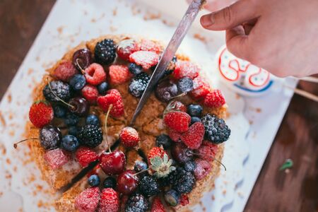 female hand cuts a raspberries blackberry birthday cake with candles number 30 on defocused background. Selective focus macro shot with shallow DOF top flat lay viewの写真素材