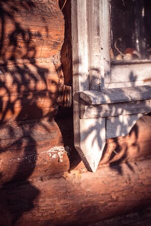 Old white painted wooden window with peeling paint from time to time on a wooden log facade lit by a bright sun casting a shadow from a tree. Selective focus macro shot with shallow Depth of fieldの写真素材