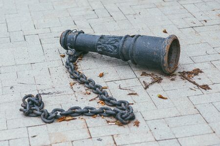 An old antique rusty, metal balustrade baluster with a heavy chain lying on a tile in a parkの写真素材