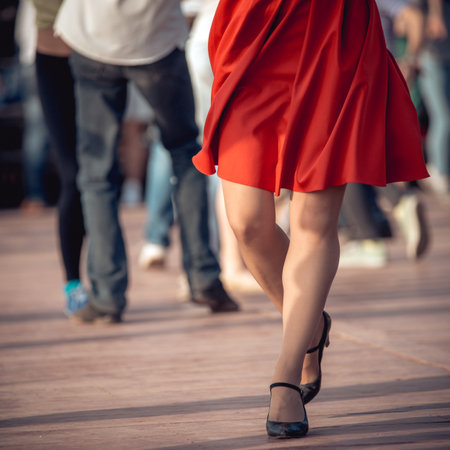 people are dancing outdoors in the park at sunny day. beautiful female feet in dancing shoes in the foreground and red skirtの写真素材