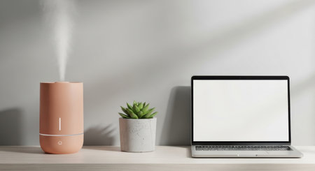 A minimalist desk arrangement with a laptop, humidifier emitting mist, and a succulent plant.の素材