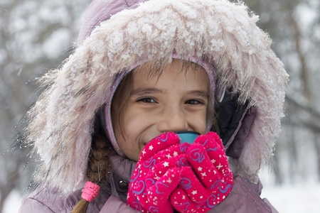Small smiling girl drink hot tea in winter park while activitiesの写真素材