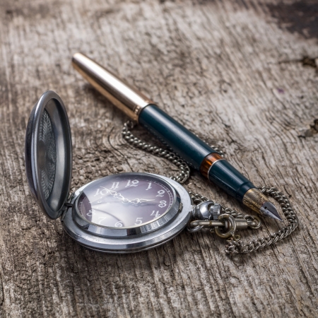Old pocket watch and fountain ink pen on wood backgroundの写真素材