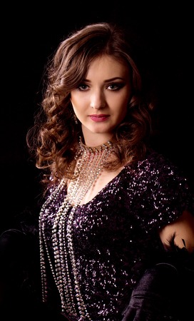 Young brunette woman in black shiny dress posing on black background