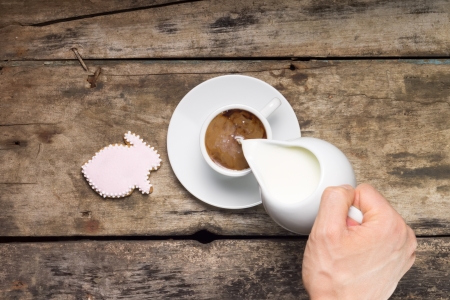 Pouring milk in White Cup of Coffee  Coffee with gingerbread rabbit on wood background  Top Viewの写真素材