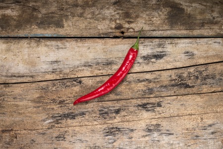 One Red Chilly Pepper on Grunge Wood board. Top View