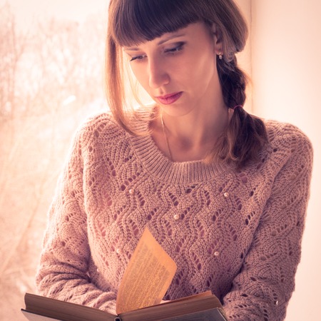 Young student girl reading book near the windowの写真素材
