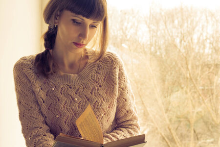 Young adult girl reading book near the windowの写真素材