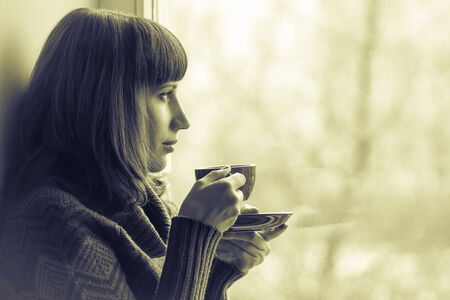 Beautiful girl drinking coffee or tea near window. Toned Imageの写真素材