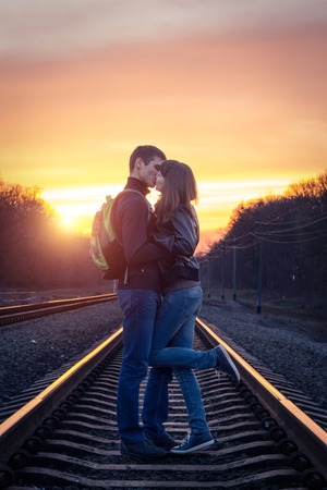 Romantic couple kissing at sunset on railroadの写真素材