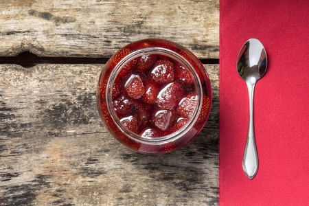 Strawberry jam with teaspoon served on wood background