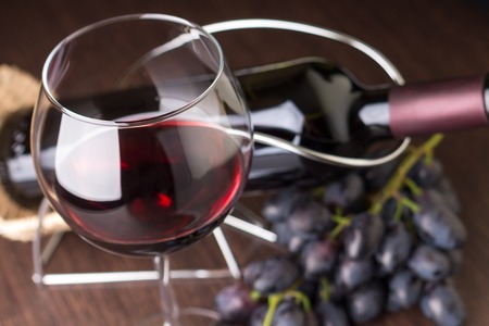 Wineglass with red wine with grapes and bottle at backgroundの写真素材