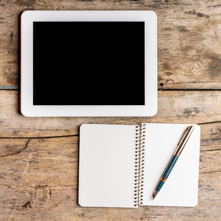 Digital pad with empty black screen and opened notebook with old fountain pen on wooden table