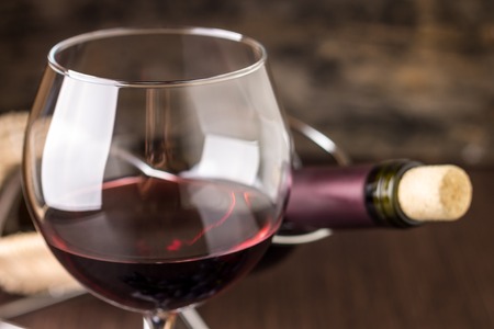 Red wine in wineglass against corked bottle on wood backgroundの写真素材